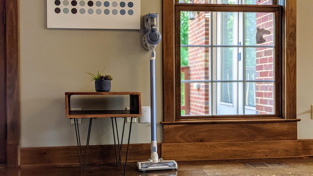 A cordless vacuum leaning against a wall, between a table and a window