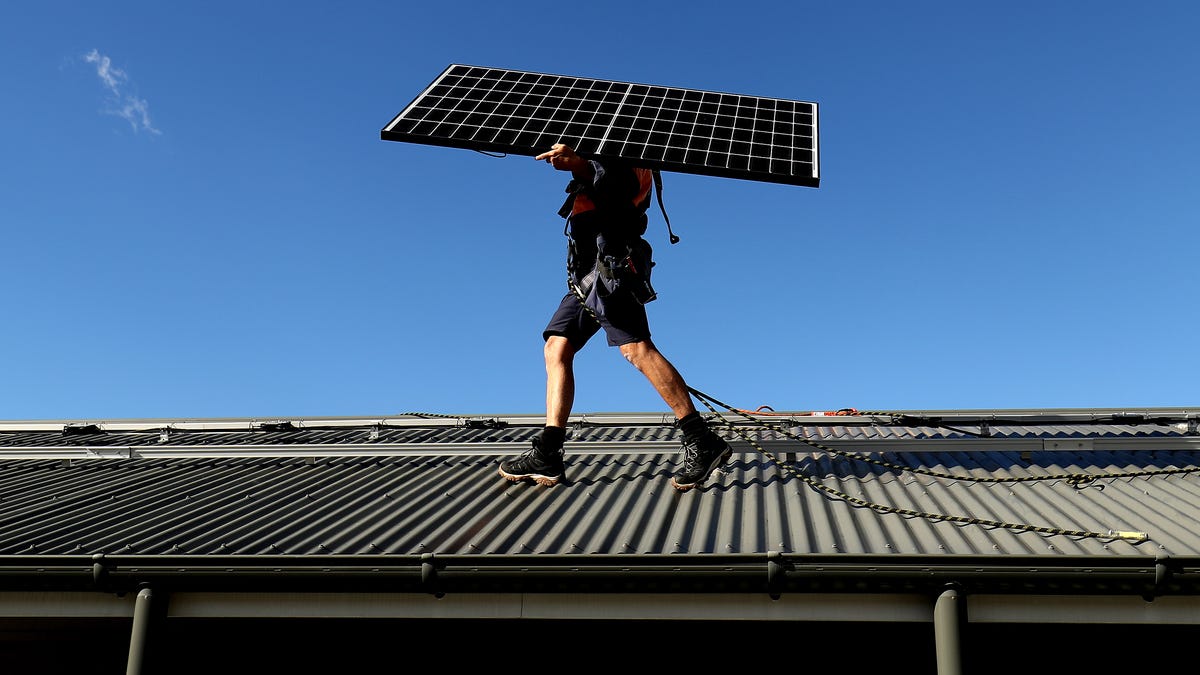 Person walking on a roof with a solar panel on their shoulder.