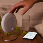 The Halo Rise device on a bedside table with a phone and water cup next to it.