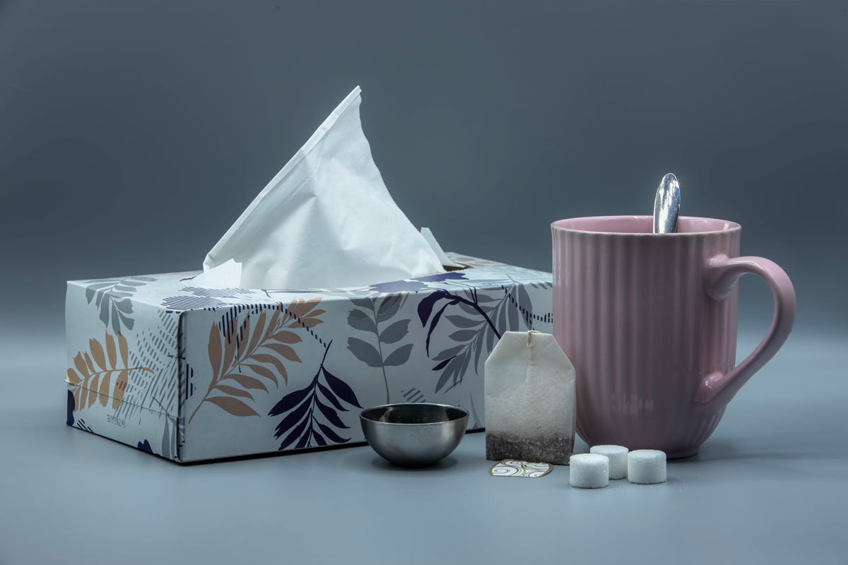 A cup of tea with a box of tissues and medicine