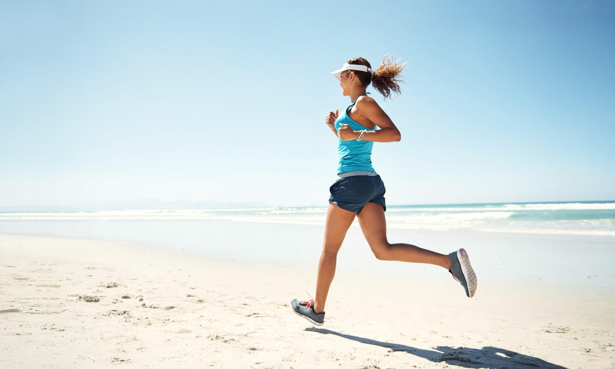 Woman runs on sunny open beach in shorts and tank top.