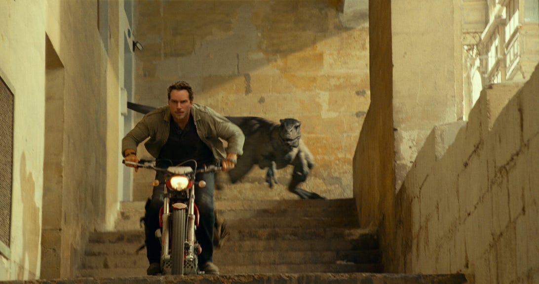 Chris Pratt'ın Owen Grady'si Jurassic World Dominion'da bir dinozor tarafından takip edilirken motosikletle taş basamaklardan iniyor