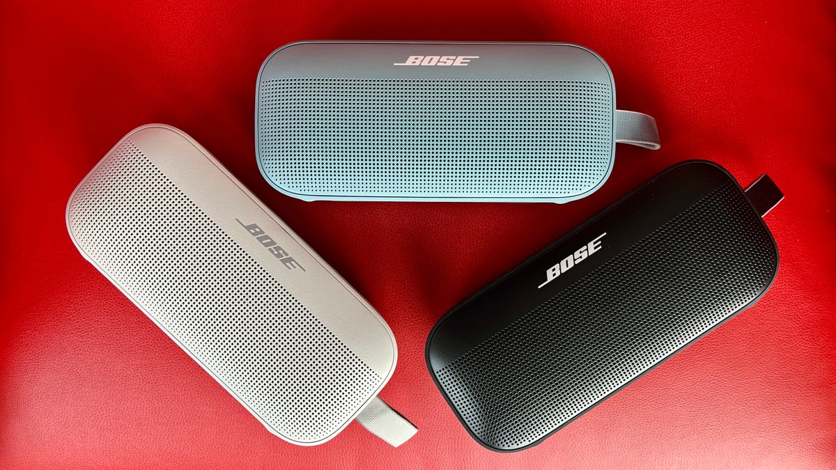 All three colors of the Bose SoundLink Flex, black, white and blue, against a red background.