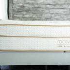 Saatva Classic King Mattress on top of a white bed frame with a wooden headboard