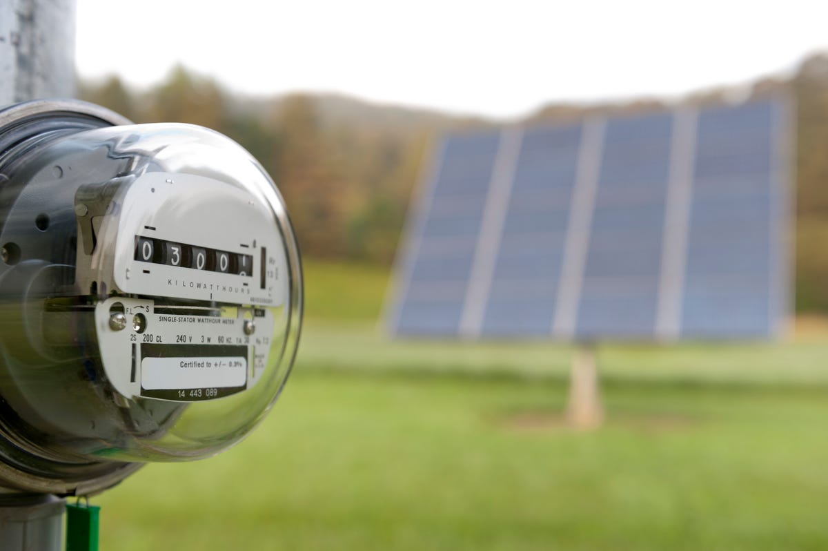 An electricity meter with solar panels in the background.