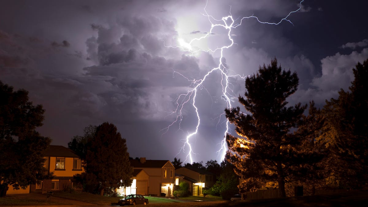 Lightning at night strikes behind homes with interior lights turned on.