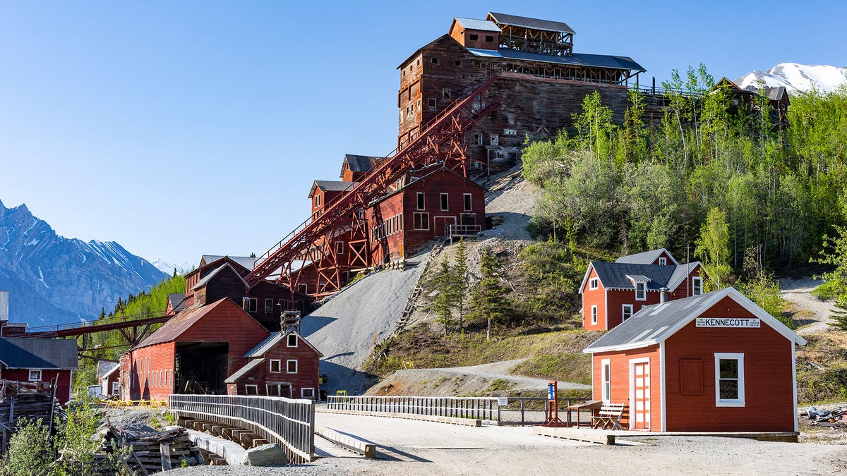 a huge wooden mine building stands on a steep wooded hillside with mountains in the background