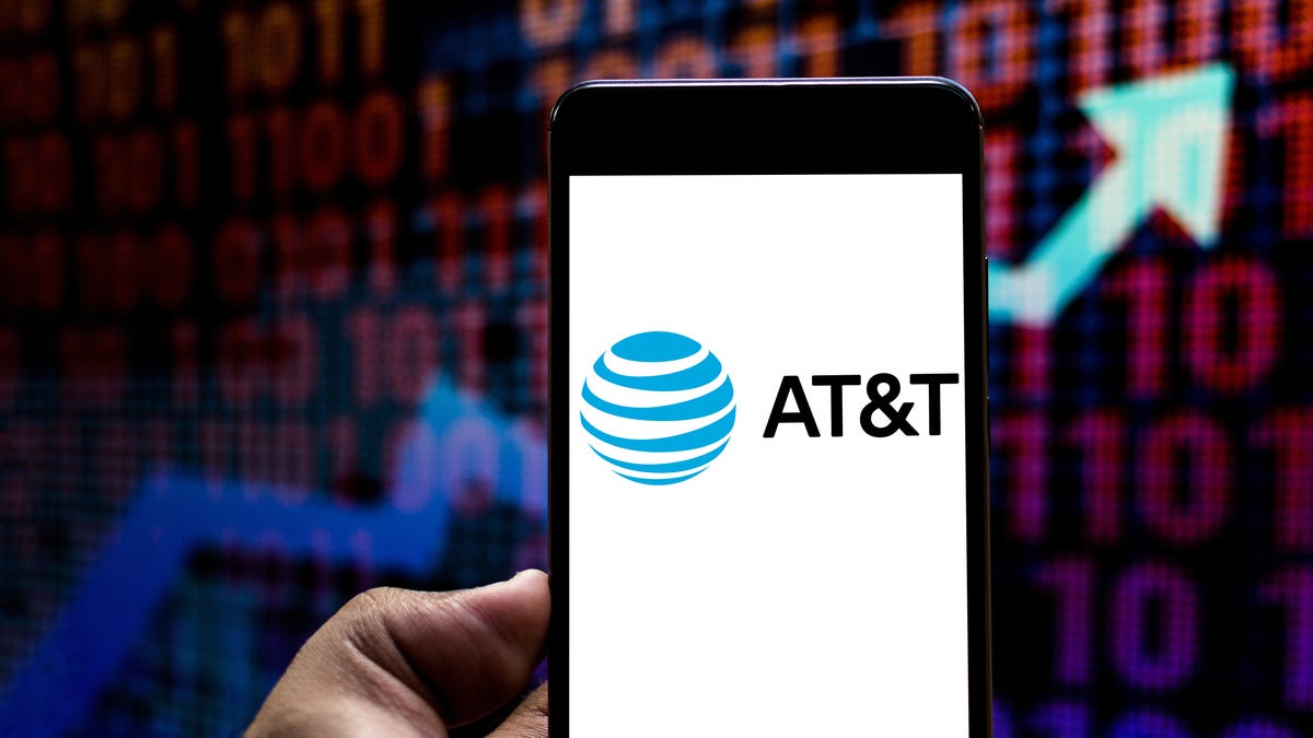A smartphone with an AT&T logo in front of a stock ticker background with an arrow going up.