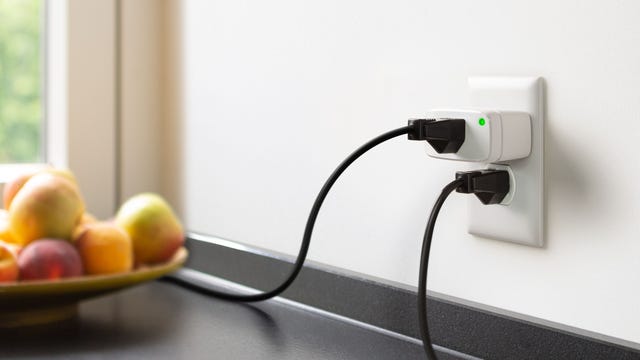 The Matter-compatible Eve Energy smart plug in the top socket of a kitchen outlet, with another cord plugged into the outlet below.
