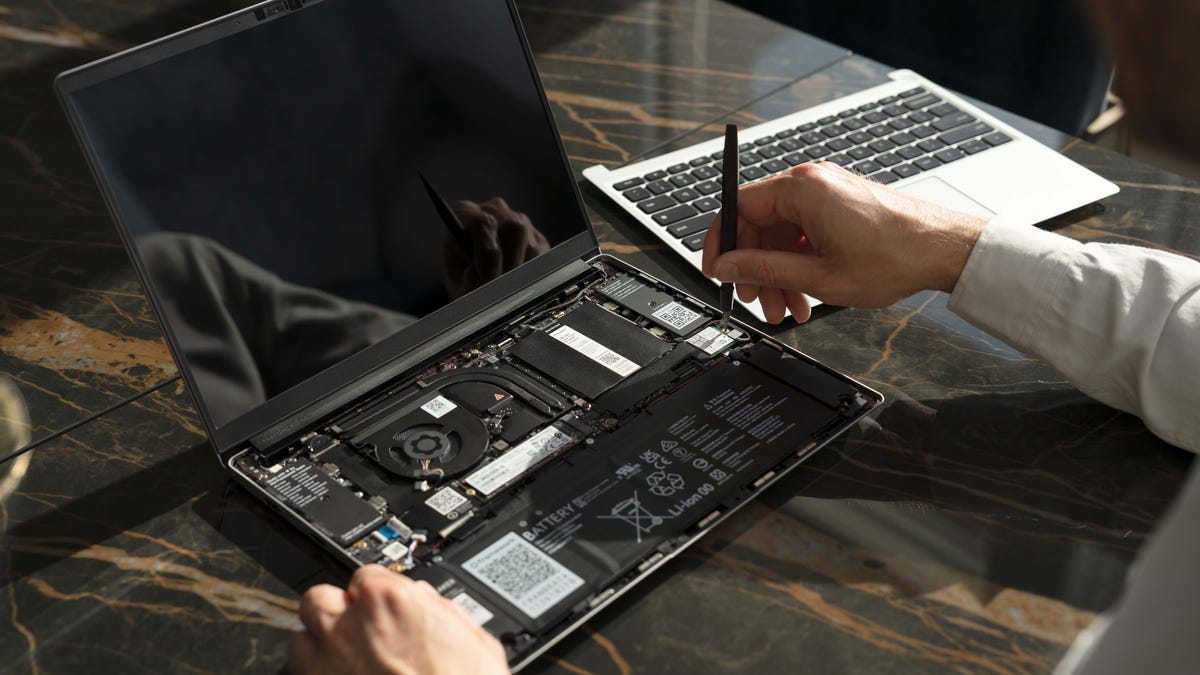 Framework Chromebook with its keyboard off and hands replacing components inside.