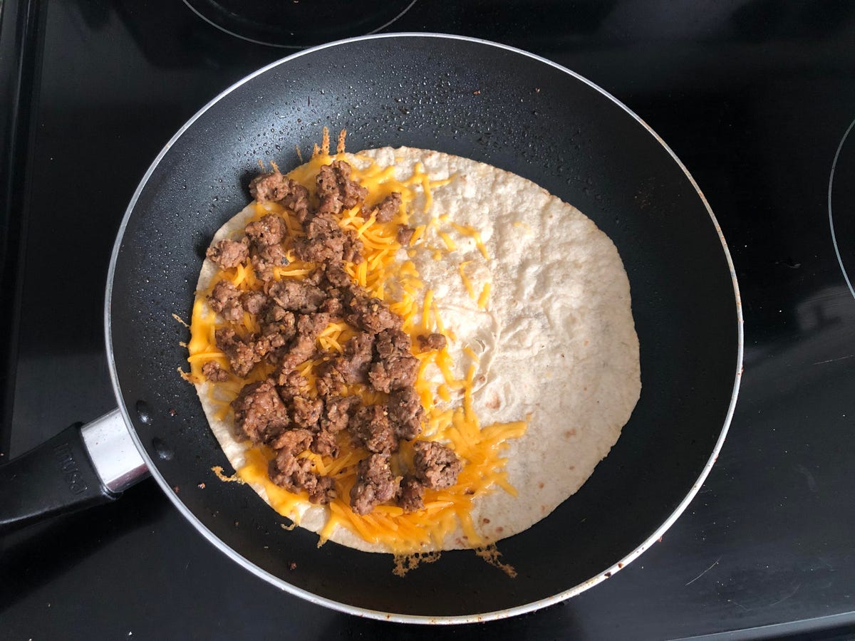 A tortilla in a pan with cheese and Impossible Burger on one half.