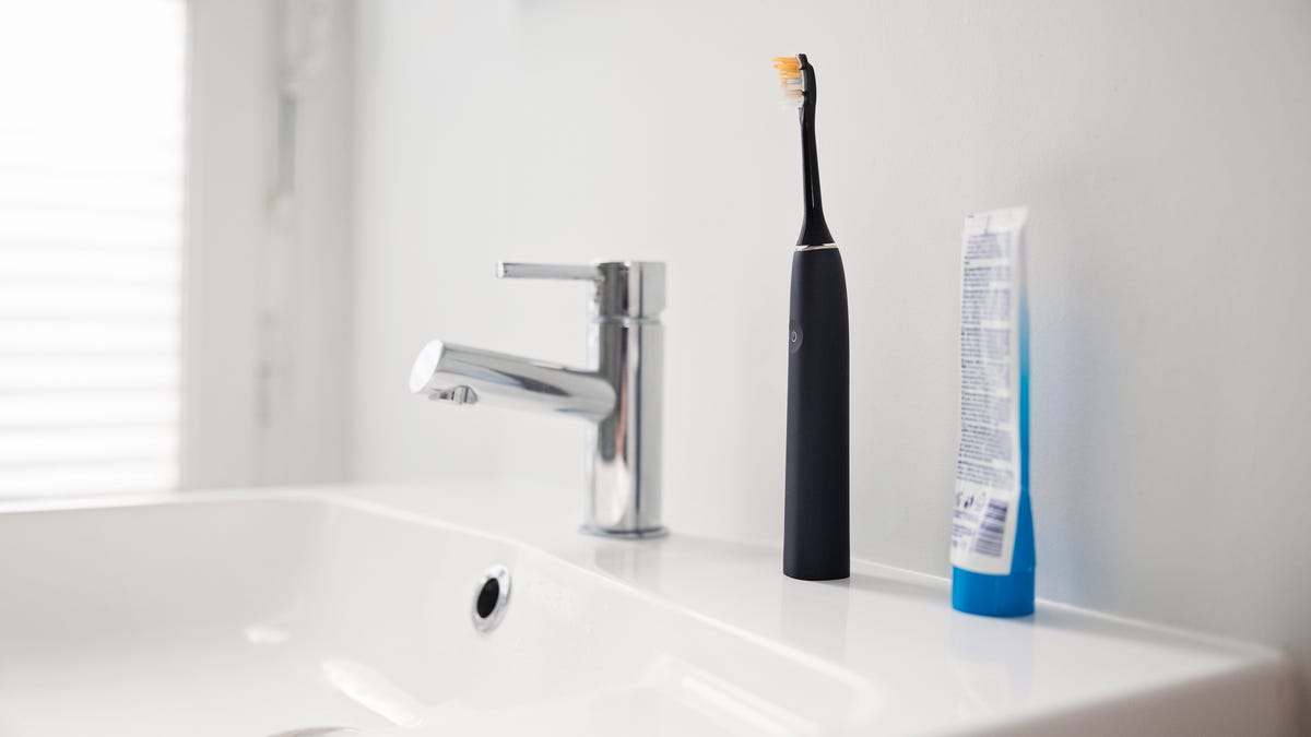 a black toothbrush on a bathroom counter next to a toothpaste tube.