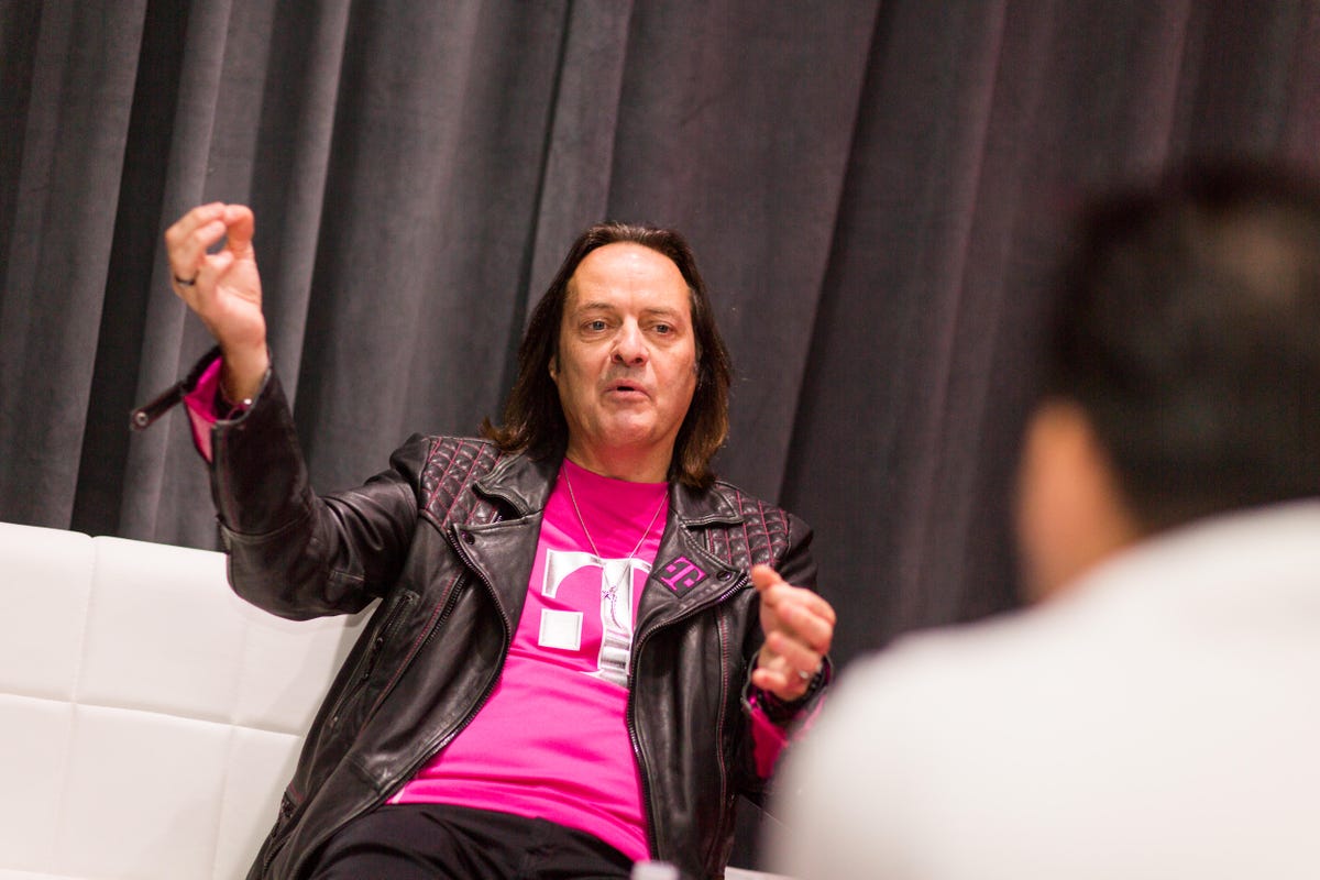John Legere gestures with his hands while speaking on a couch