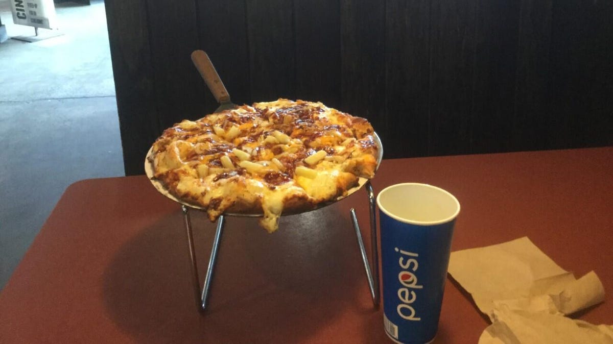 A barbecue chicken pizza on a serving tray, next to a cup with 