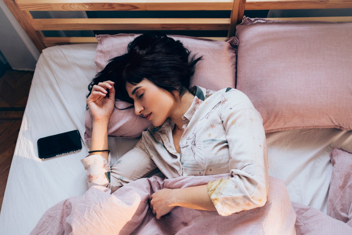 Woman sleeping in bed while using a sleep app on her phone.