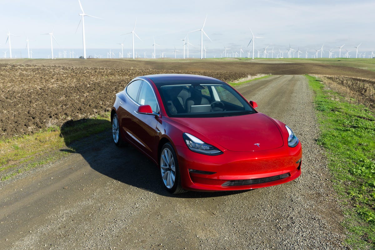 2018 tesla model 3 parked across a country road with a wind farm in the background