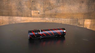 A red and black Olight Baton Pro 3 flashlight sits on a black tabletop in front of a wooden background.