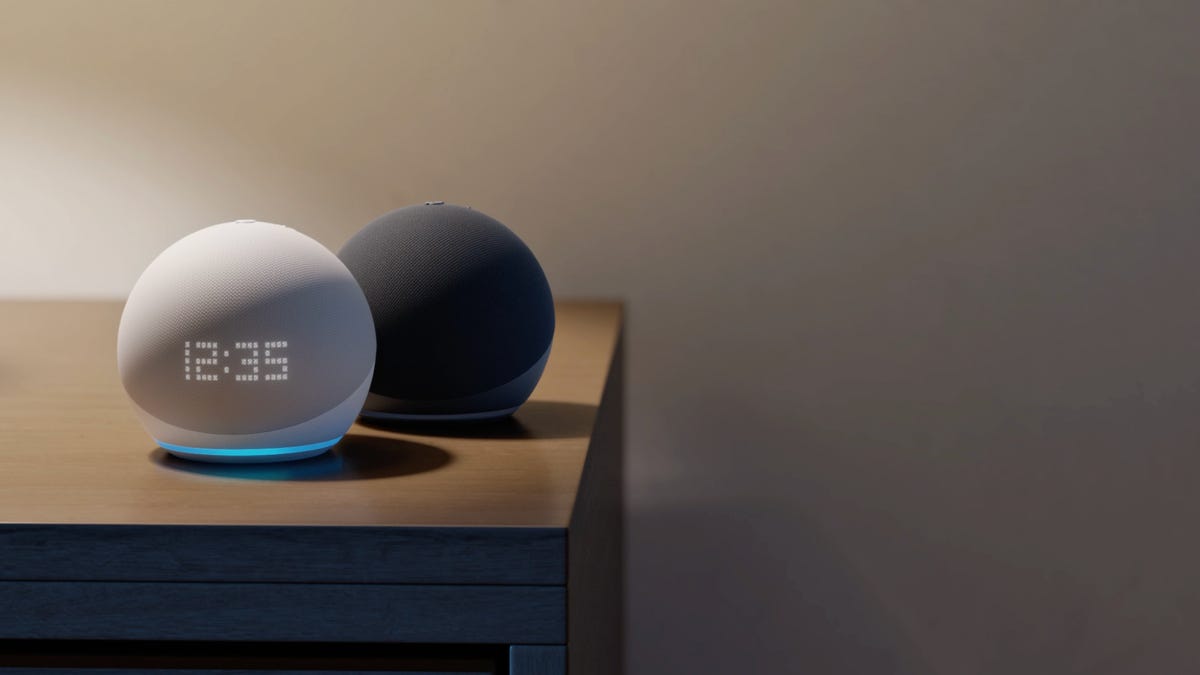 El Amazon Echo Dot de quinta generación y el Amazon Echo Dot con reloj sentados en una mesita de noche junto a la cama.