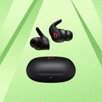 A black pair of Beats Fit Pro earbuds against a green background.