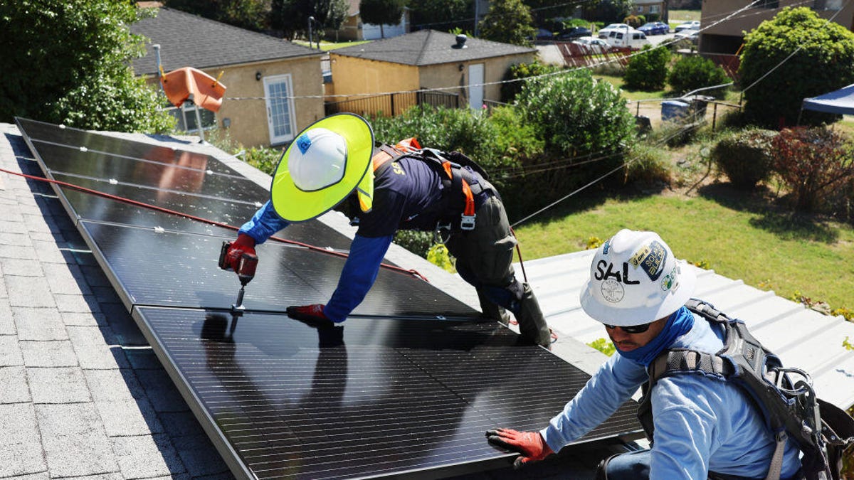 Two workers install solar panels on top of a house.