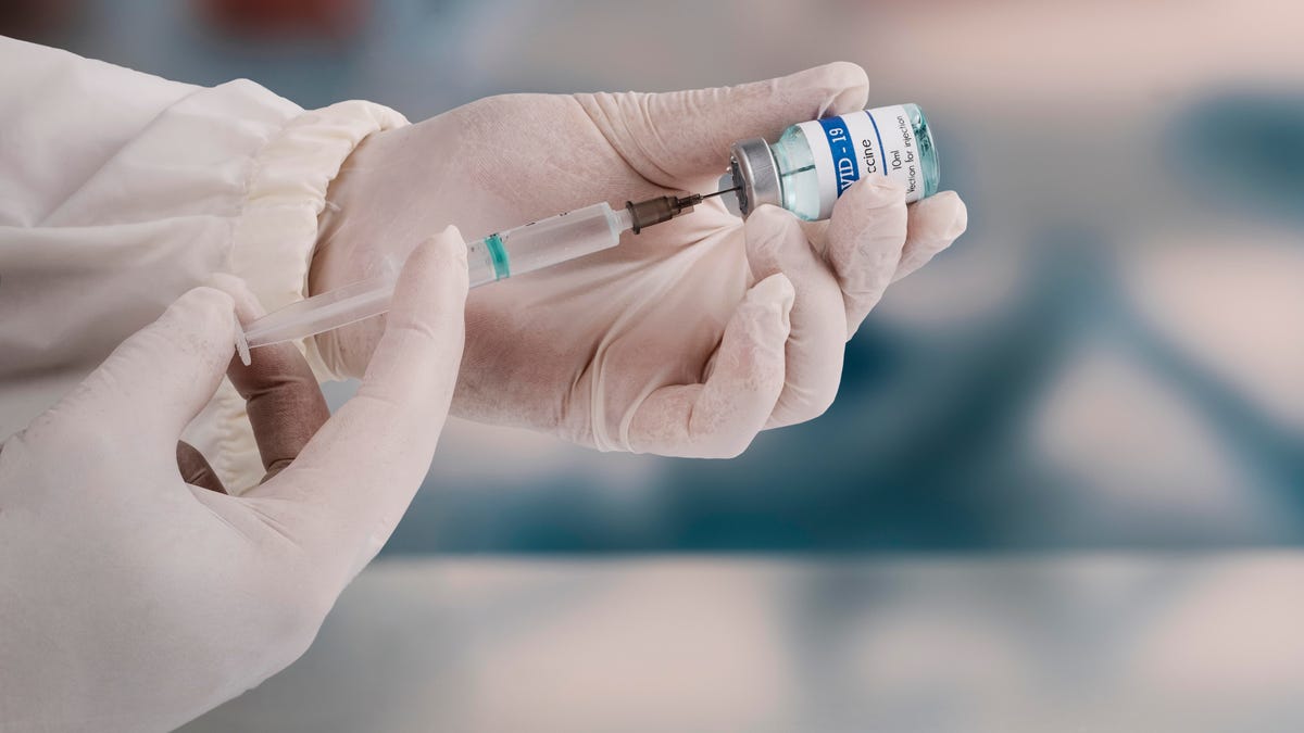 Gloved hands use a syringe to extract a dose of COVID-19 vaccine from a vial