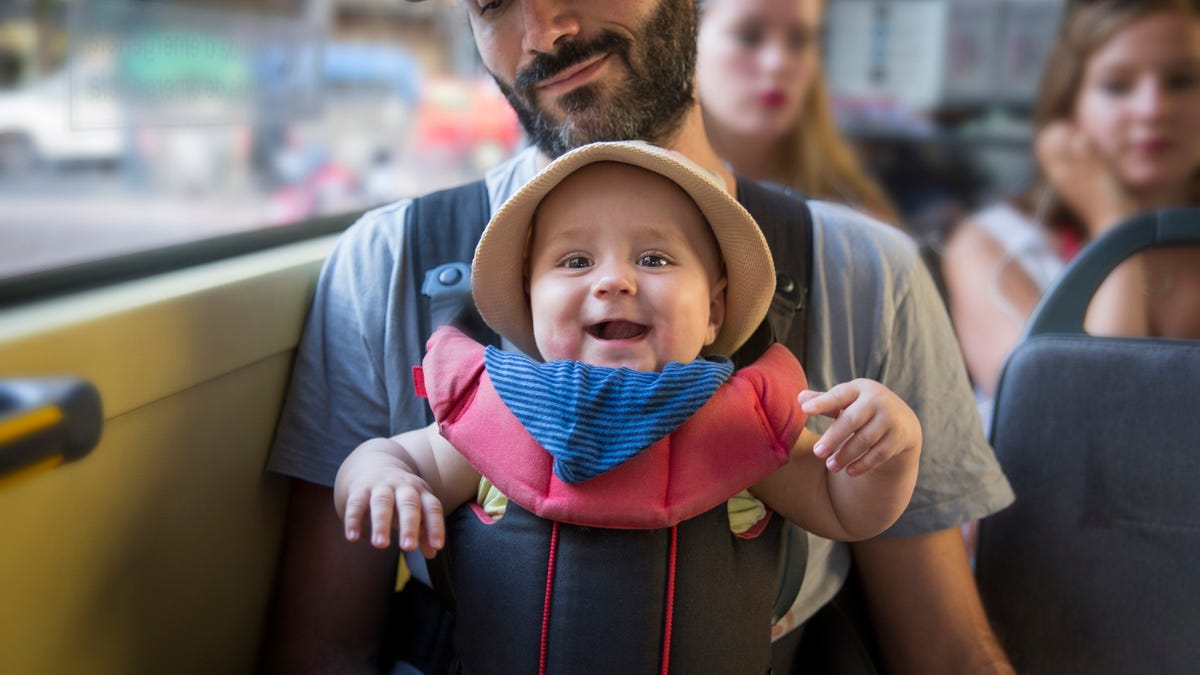 Man "wearing" a smiling baby in a forward-facing carrier