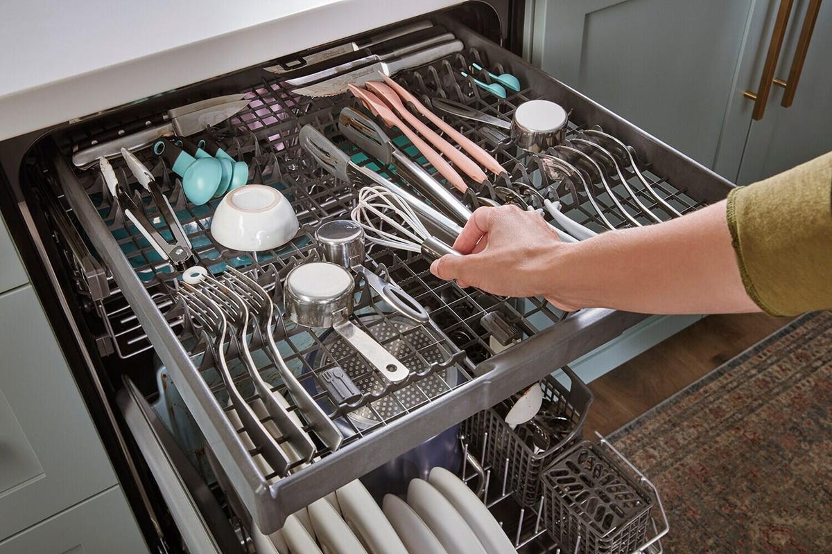 A person places a small whisk in the third rack of a dishwasher