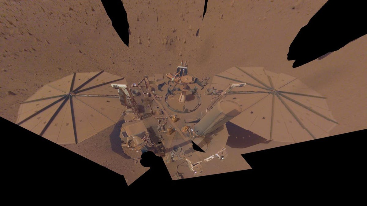 InSight lander with its umbrell-like solar panels is seen coated in dust on the rocky surface of Mars.