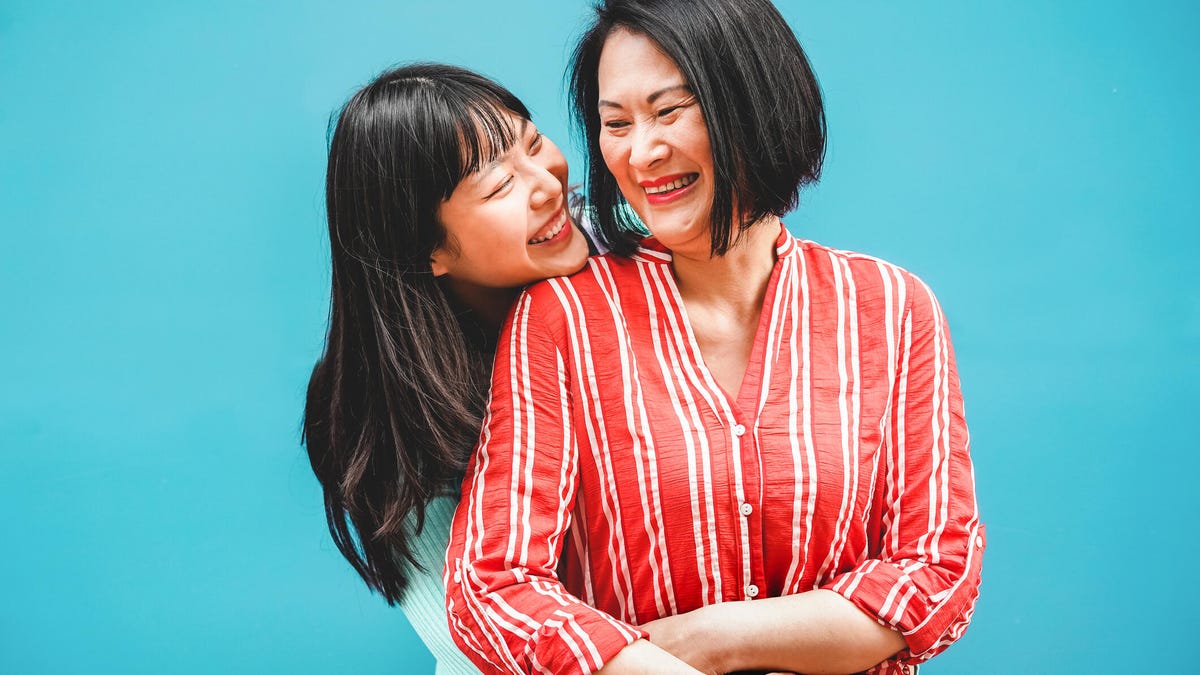 Asian mom and daughter hugging and smiling in front of a bright blue backdrop.