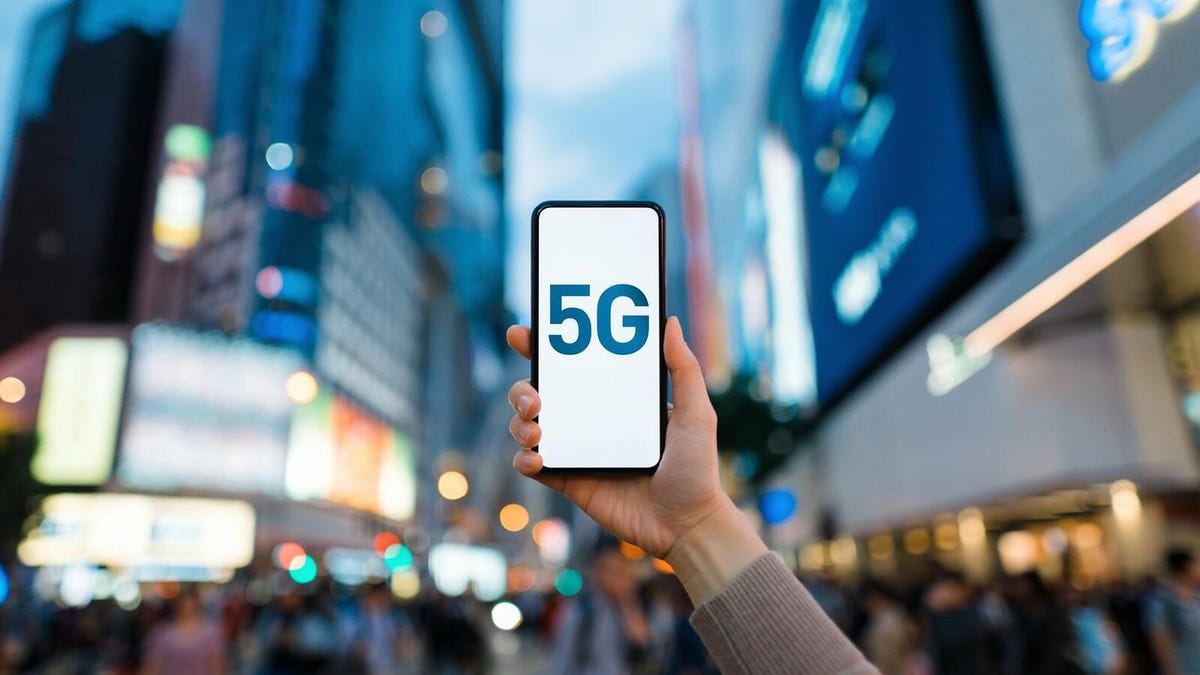 A phone displaying '5G' in front of a blurred city background.