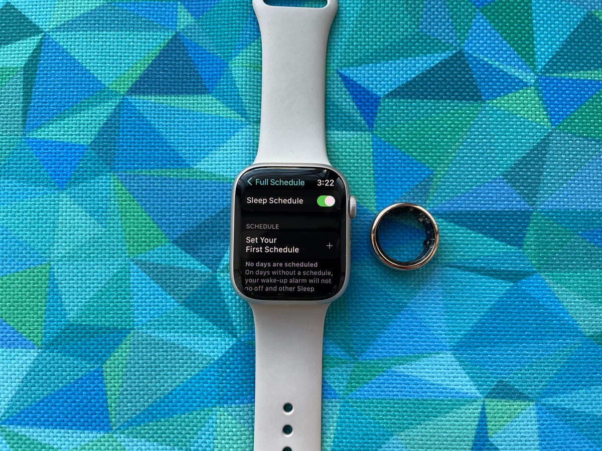Apple Watch Series 8 next to Oura ring on a blue patterned background