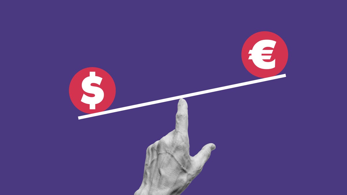 A finger holding the symbols for the dollar and euro on a balance