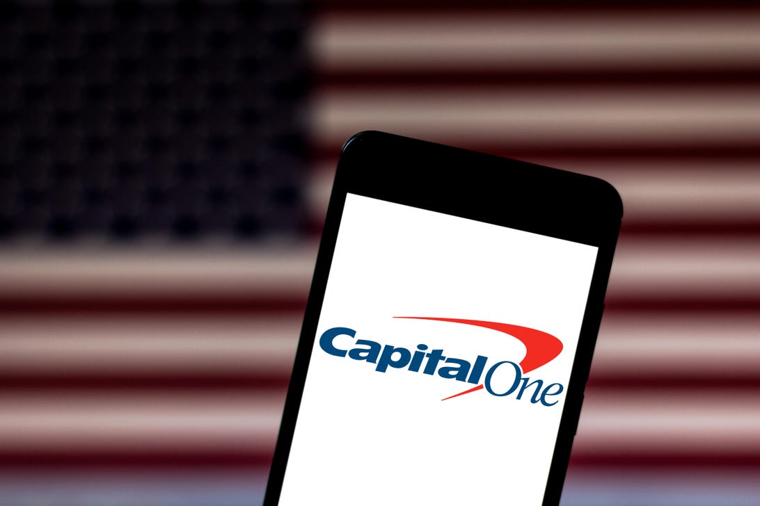 The Capital One logo is visible on a phone screen with the American flag in the background.