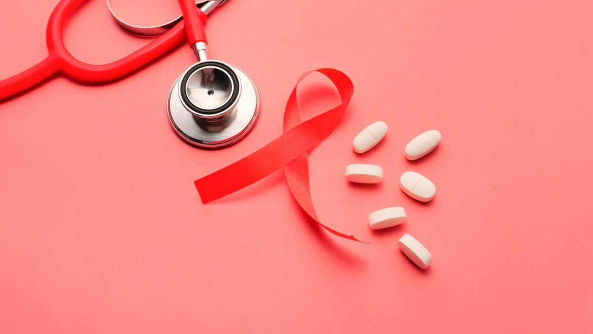 A stethoscope, red ribbon and pills against a light pink background