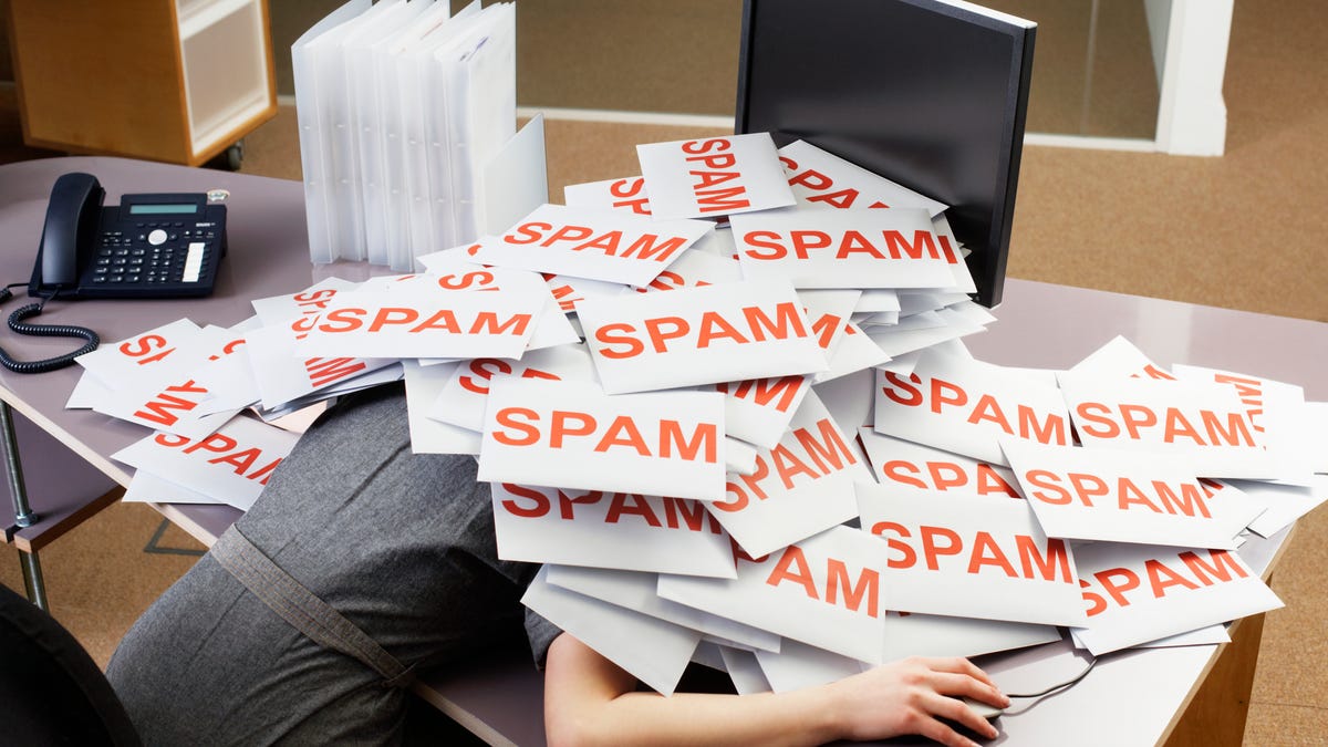 Person under a pile of papers which have the word "SPAM" printed on them in orange