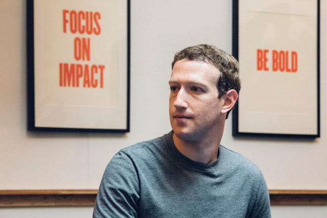 Facebook CEO Mark Zuckerberg, in front of signs that say "Focus on Impact" and "Be Bold."