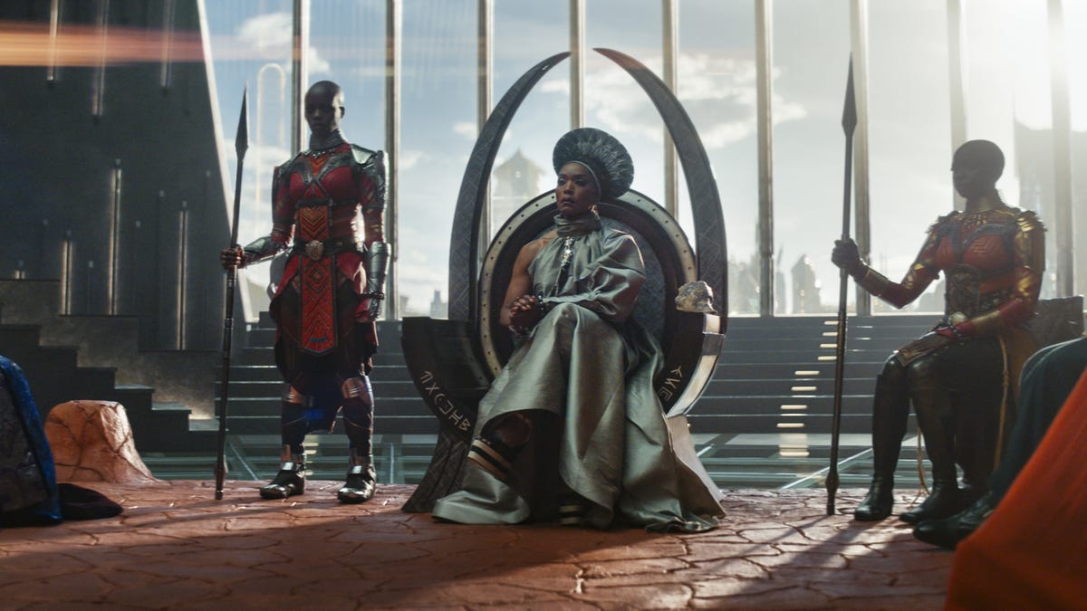 Queen Ramonda, played by Angela Bassett, sits on the Wakanda throne surrounded by warriors and members of court.