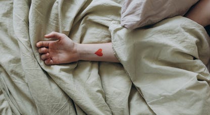 A person's arm poking out of the sheets with a heart tattoo
