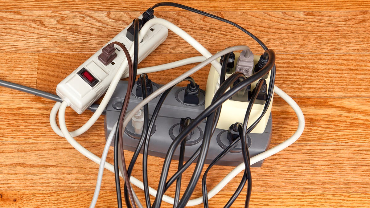 A power strip sits on a wooden floor with way too many plugs in it.