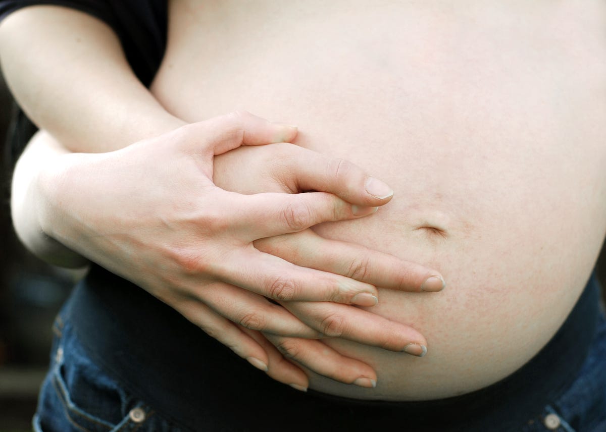 A close-up of a pregnant belly, with two interlinked hands embracing it.