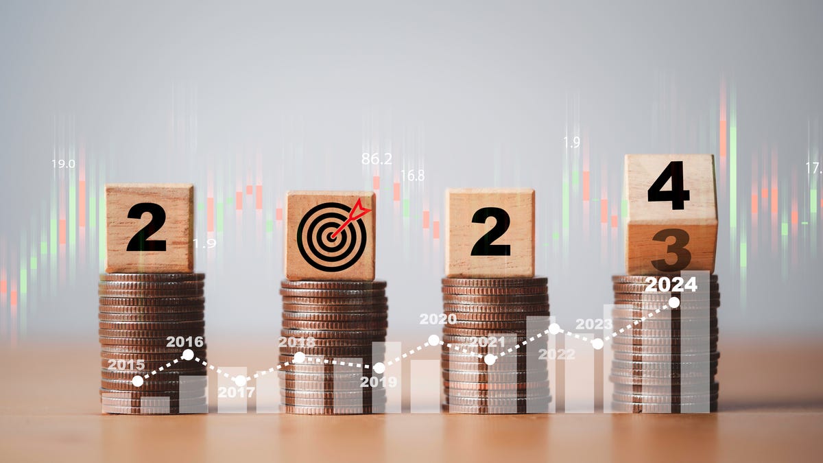 the year 2024 is displayed with wooden blocks on top of stacks of coins. the zero in 2024 is a target, and the 4 is rolling over from 3 to show the change from 2023 to 2024