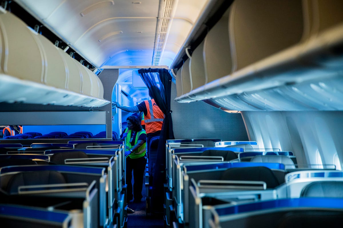 In the cabin of a Boeing 777, cleaning crews vacuum the floor and check the overhead bins for left items.