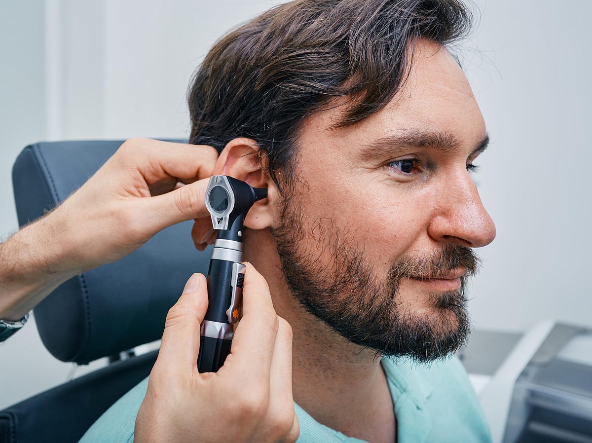 Audiologist examining male patient's ear using otoscope
