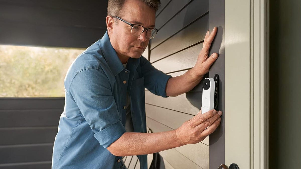 Google&apos;s Nest Doorbell, being installed beside a door by an older man.