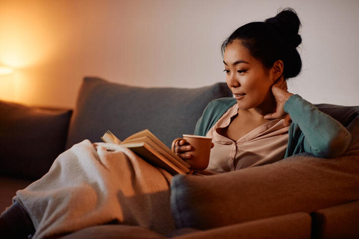 Woman dinking tea while reading a book on the sofa in the evening.