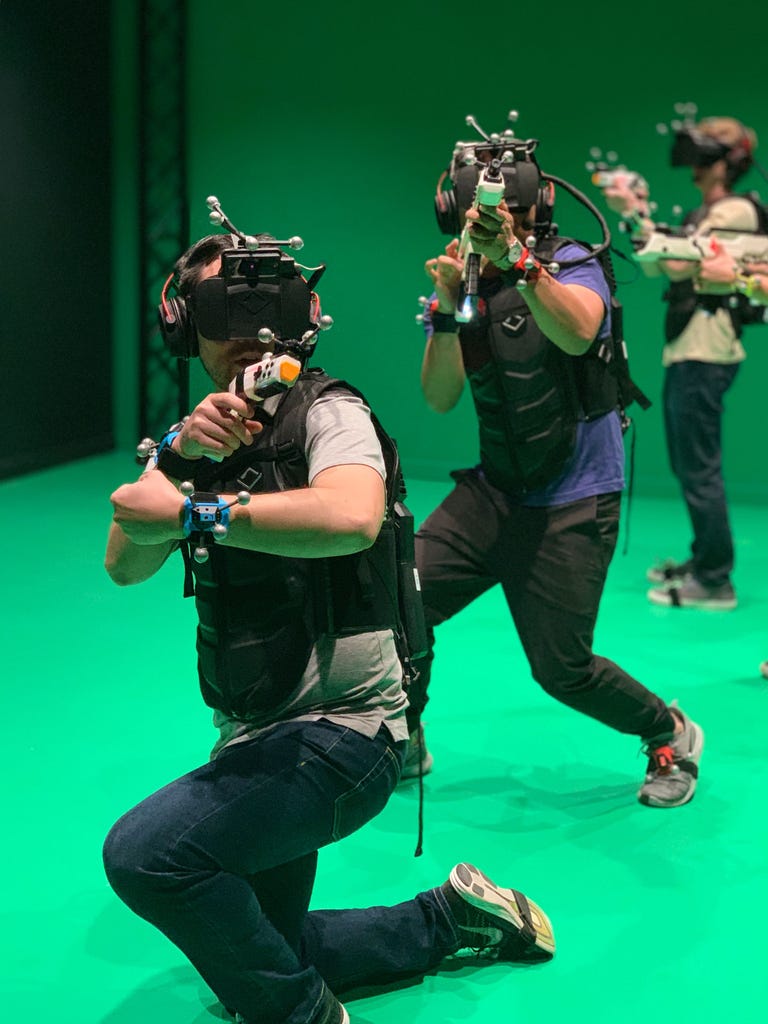 People wear VR headsets, haptic vests and laser guns
