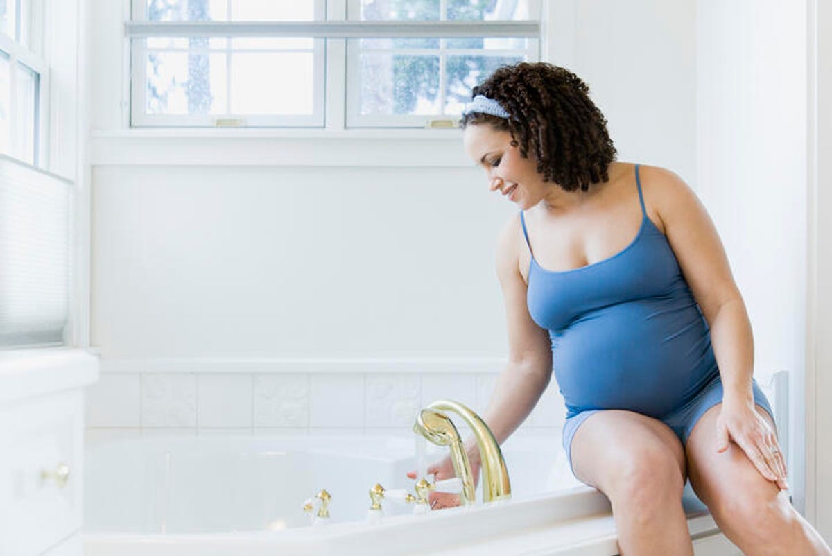 Pregnant woman sitting on the edge of the tub and testing the temperature of the water with her hand