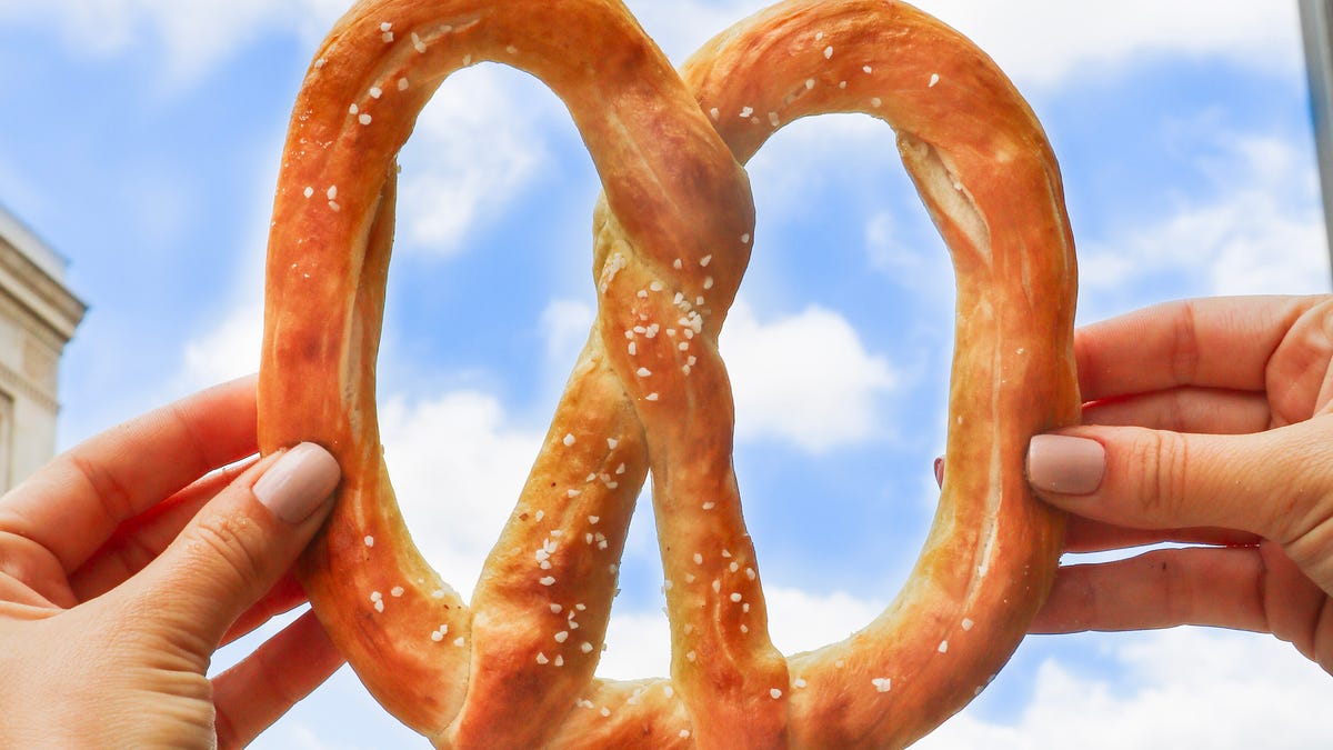 hands holding a big soft pretzel against the sky