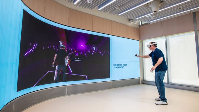 Inside Meta's store, a man wearing a VR headset stands in front of a wall-sized LED screen