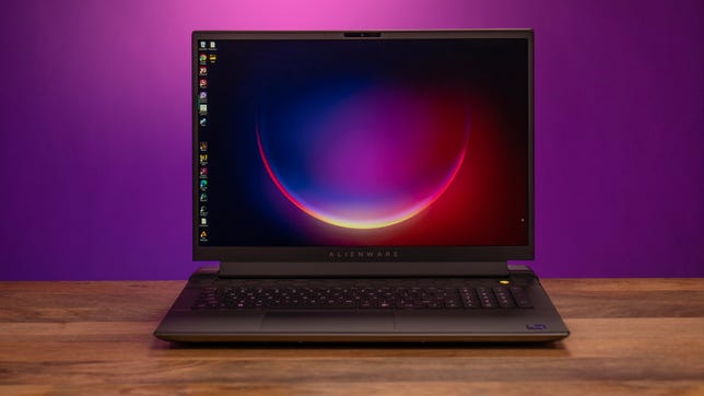 Alienware m18 R2 open, facing you, on a wood table with a magenta and purple background
